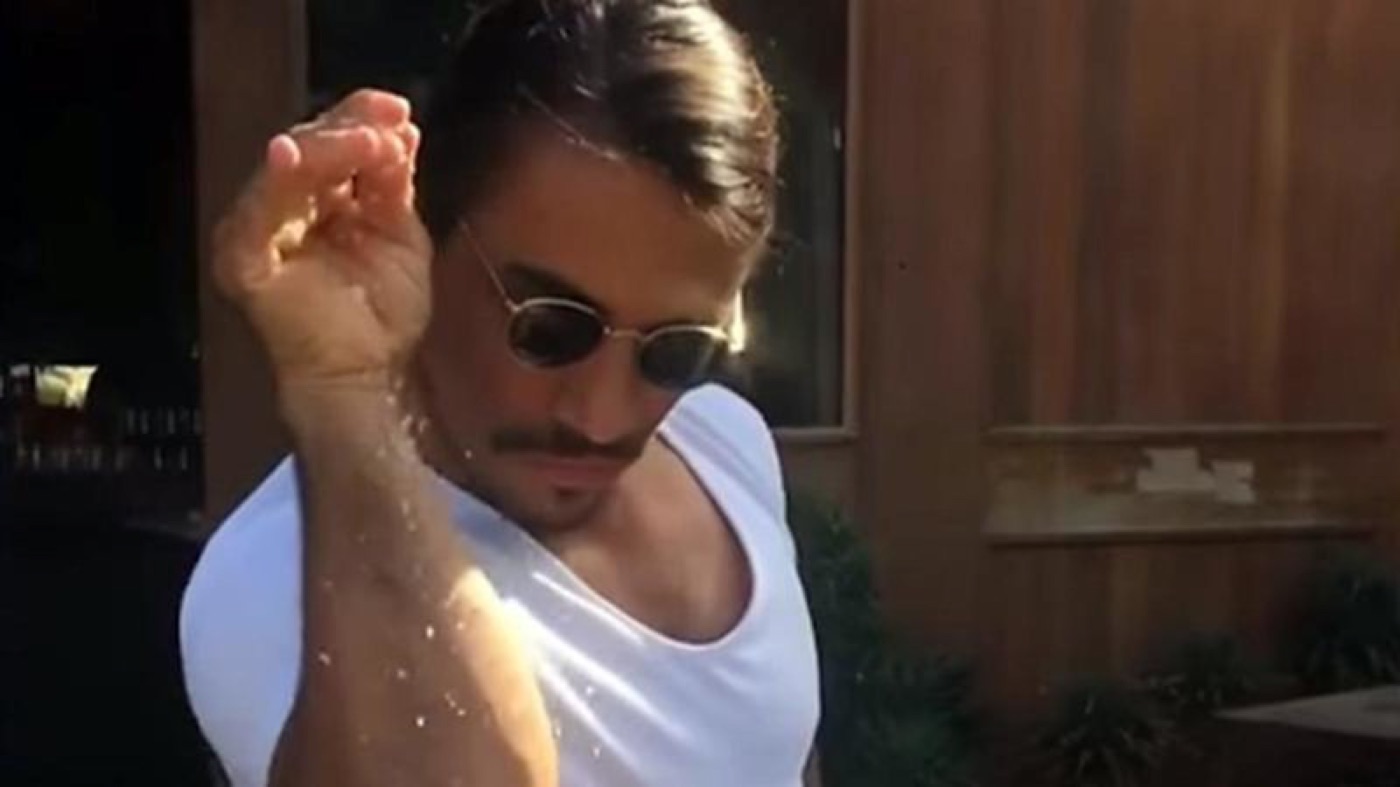 Salt Bae in sunglasses sprinkling salt down his bent forearm