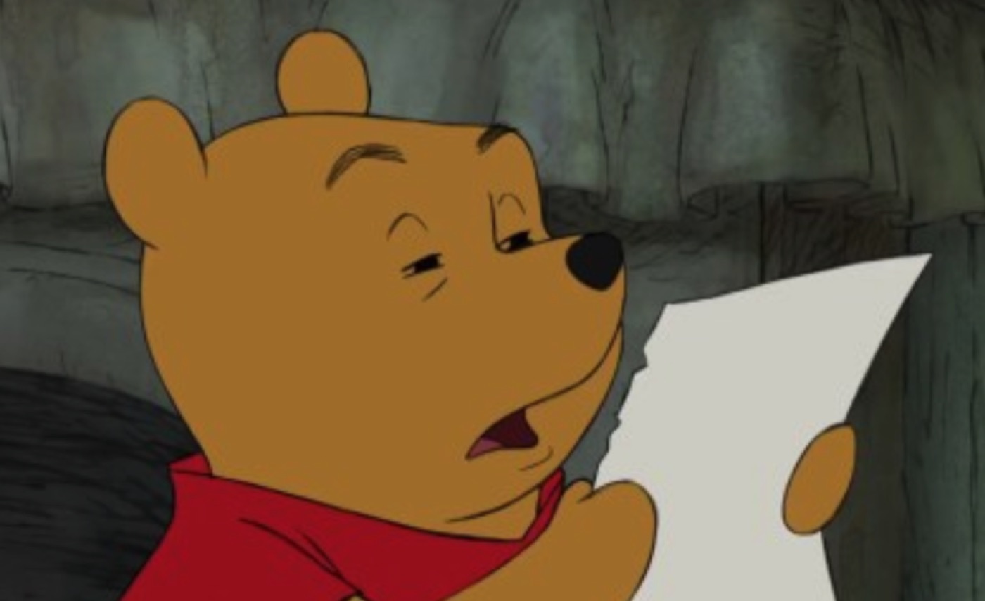 Cartoon yellow bear in a red shirt squinting at a sheet of paper, mouth slightly open in puzzlement
